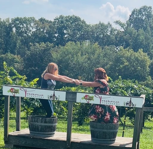 Cheryl and Denise holding hands in grape stomping buckets at a vineyard